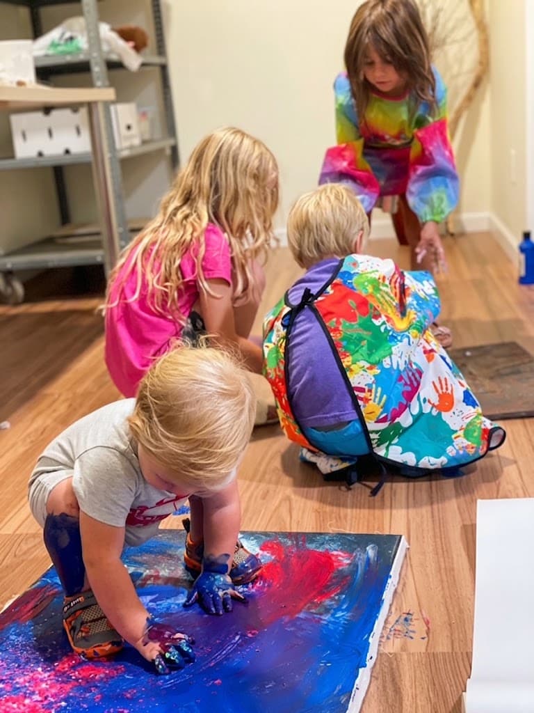 Four children working together around a canvas on the studio floor, hands covered in paint