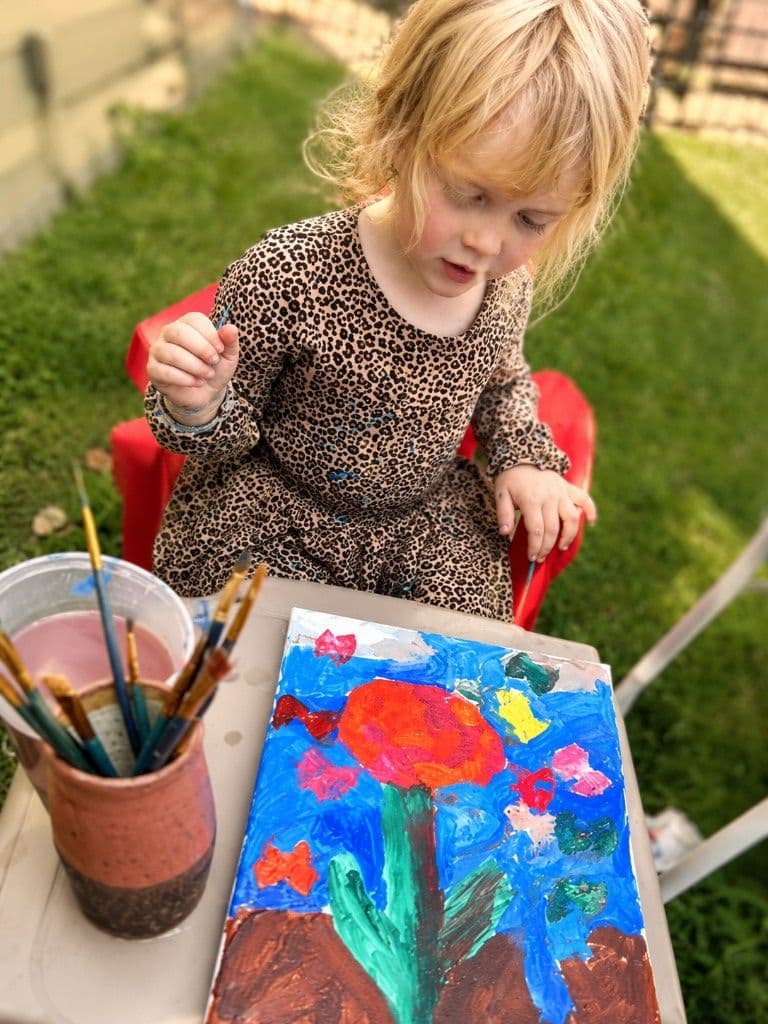 A girl outdoors in a leopard-print dress, painting a canvas of a red flower