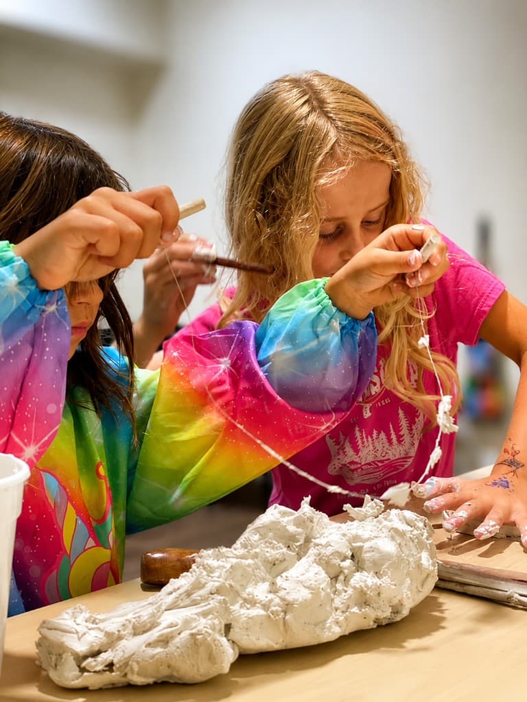 Two girls in tie-dye smocks pulling wet plaster strips with their hands
